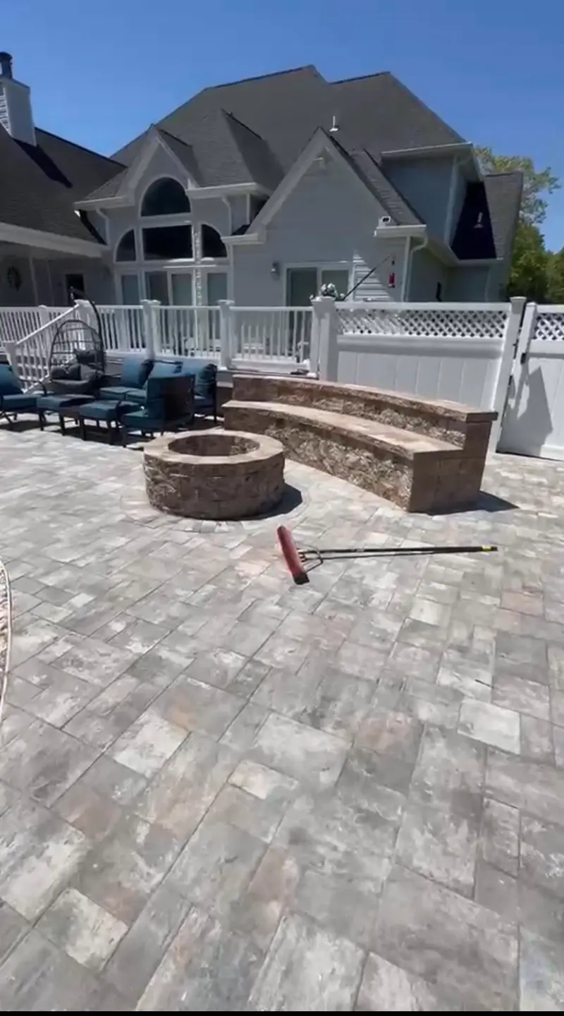 Backyard paver patio installation with stone fire pit and curved bench seating
