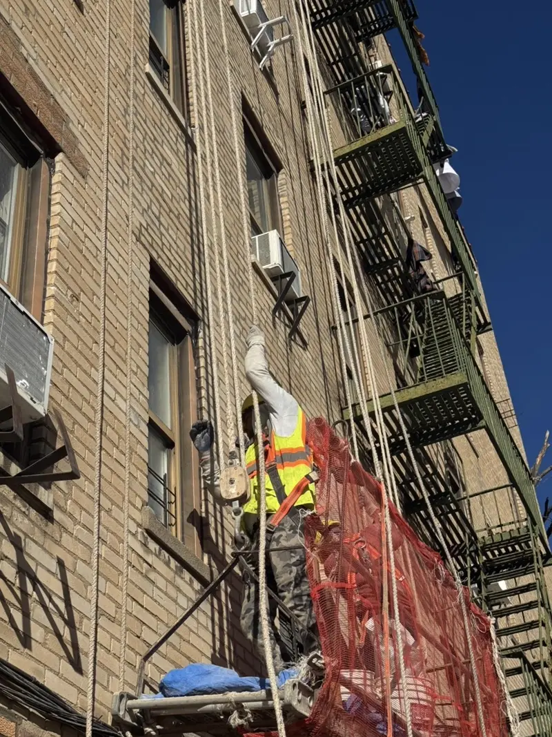 Worker performing rope access facade restoration on a Bronx apartment building
