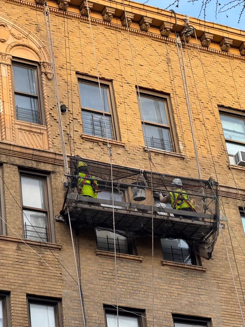 Two workers on suspended scaffold performing exterior restoration on an ornate brick building